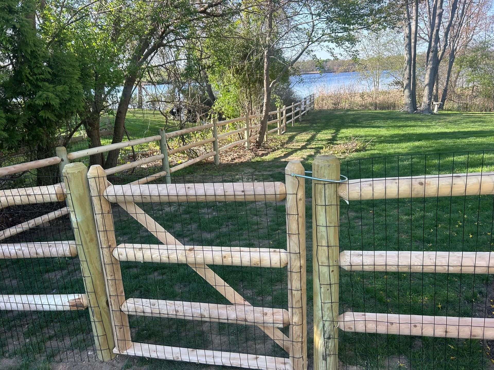 Wooden fence gate in a grassy yard with trees and a lake in the background
