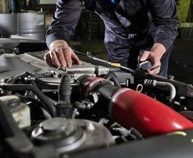 A man is working on the engine of a car in a garage.