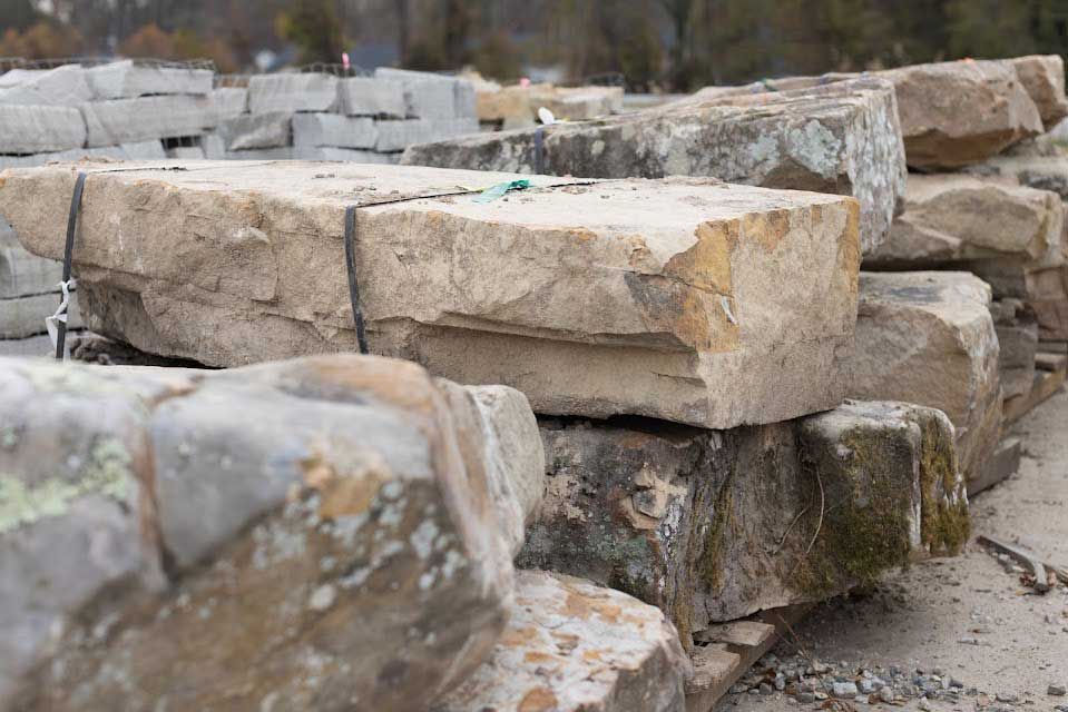 Stacked, beige, rectangular stones with rough, mossy surfaces; outdoor setting.