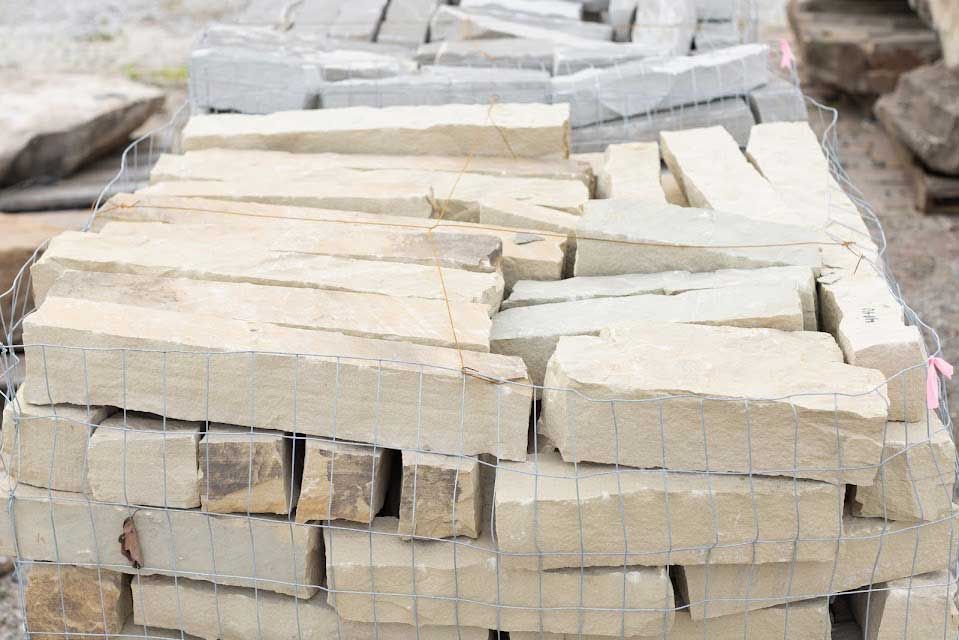 Pile of beige rectangular stone blocks wrapped in wire mesh.