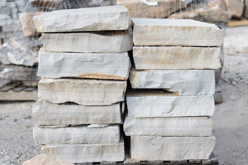 Stacked rectangular light-colored stone pavers; outdoor setting.