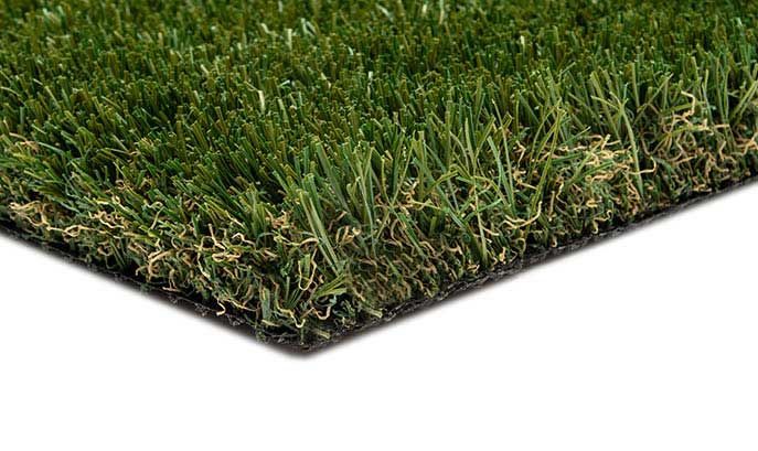 Artificial turf, showing green and tan blades with a black backing, angled over a white surface.
