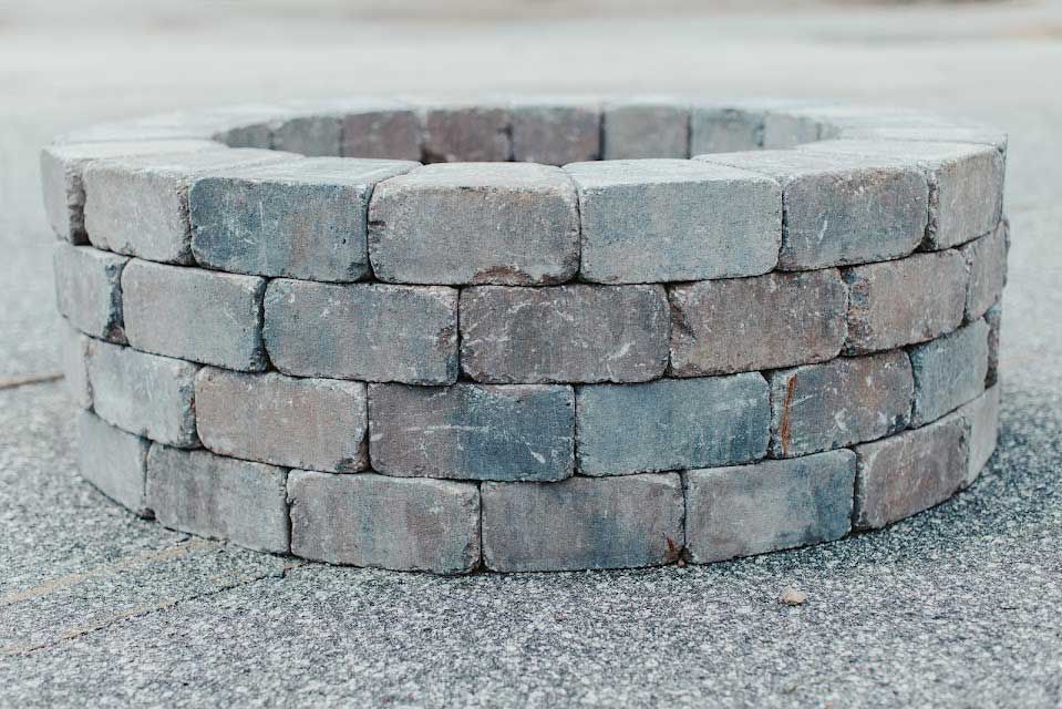 Circular brick fire pit on a gray surface, with three layers of multi-colored bricks.