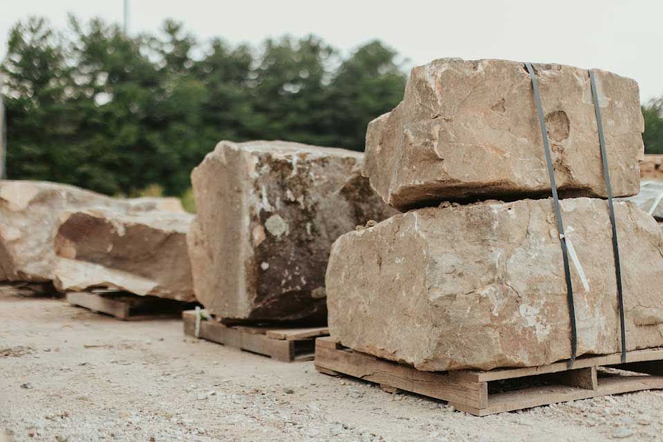 Large, rough-cut stone blocks stacked on wooden pallets, outdoors.
