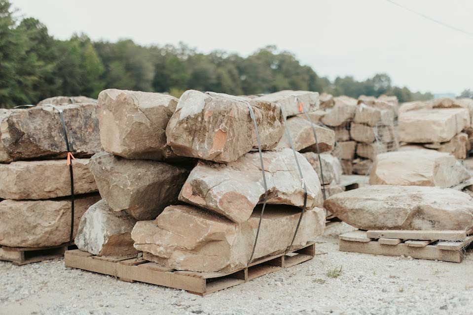 Piles of large, beige rocks stacked on wooden pallets, outdoors.