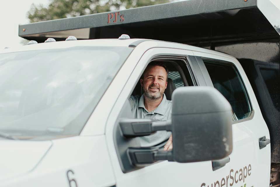 Man smiles in the driver's seat of a white dump truck,