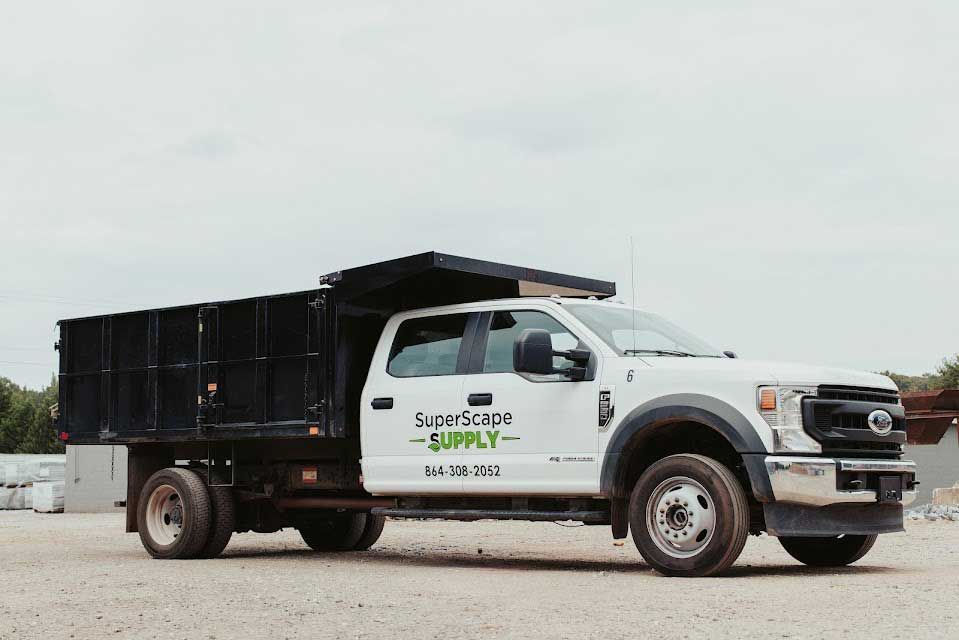 White dump truck with a black bed parked on gravel.