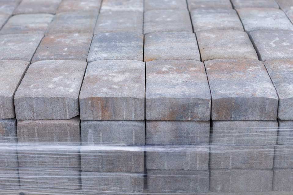 Stacked gray and brown rectangular pavers wrapped in clear plastic.