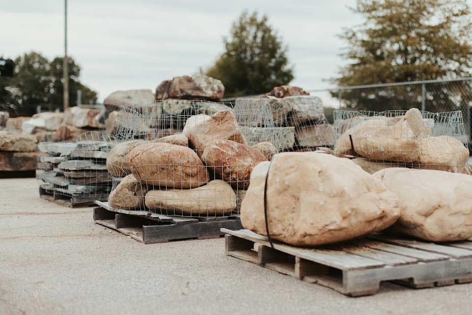 Stone landscaping rocks on wooden pallets, arranged outdoors.