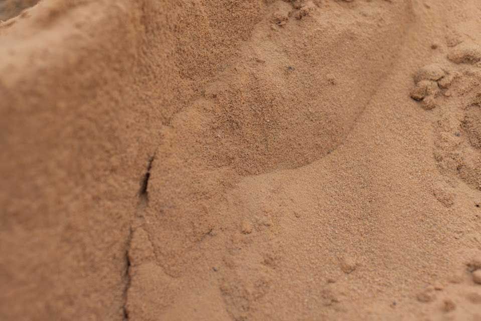 Close-up of tan-colored sand with subtle texture and shadows.