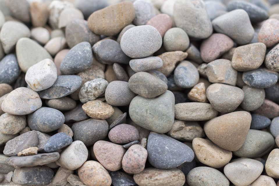 Pile of smooth, rounded river rocks in various muted colors: gray, tan, and pink.