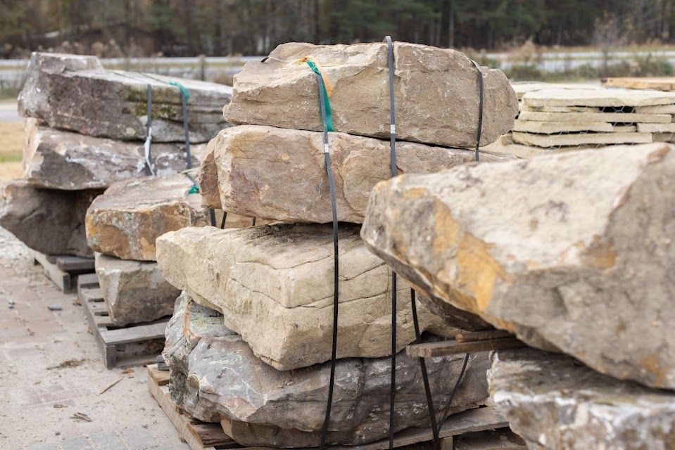 Stacked, rough-cut stone blocks secured with straps on wooden pallets, outdoors.