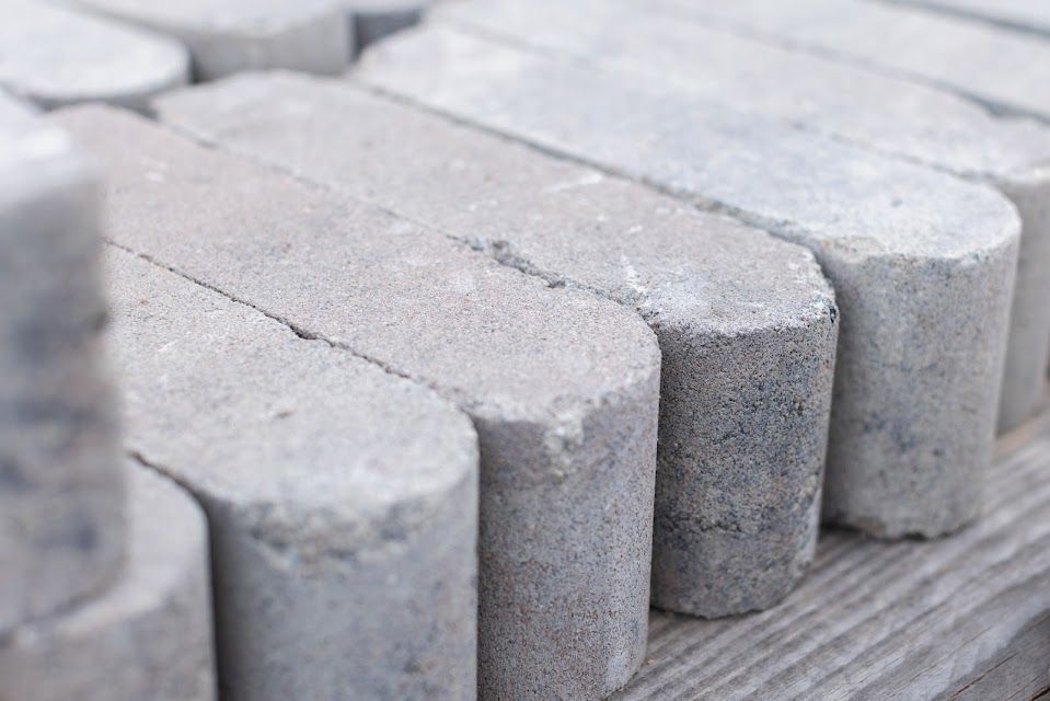 Gray, rounded-edge concrete pavers stacked on a wooden surface, ready for installation.