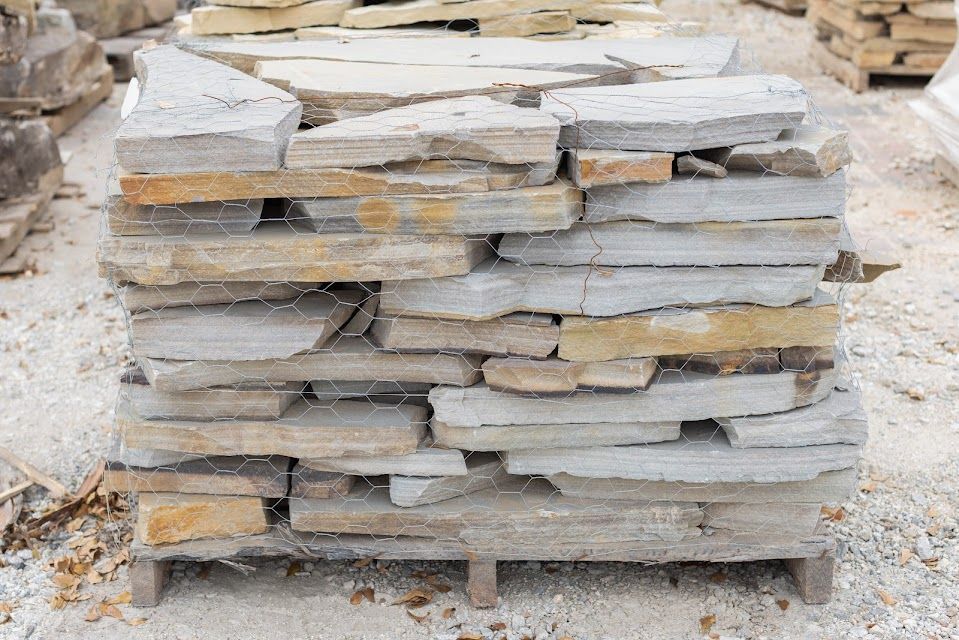 Stack of irregularly shaped gray and tan flagstones on a wooden pallet, held together with wire mesh.