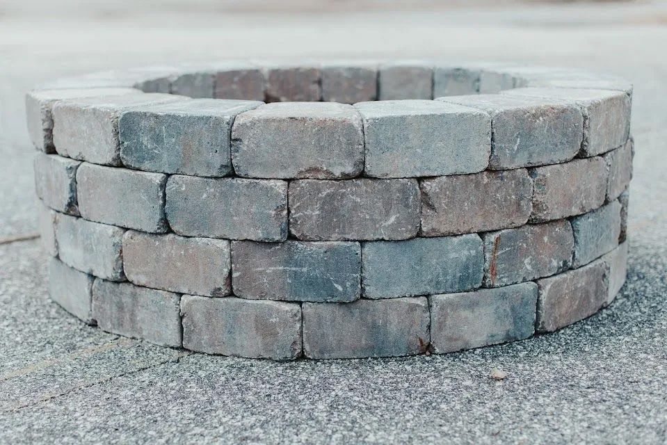 Circular fire pit constructed of grey interlocking bricks.