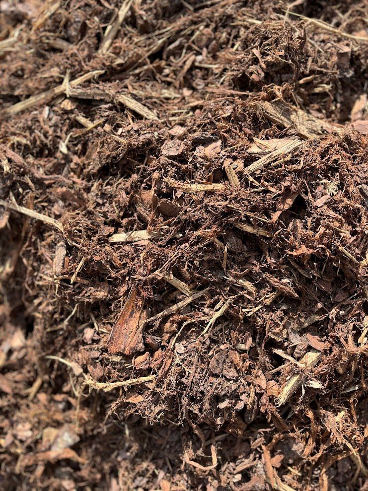 Close-up of dark brown mulch, containing wood chips and straw.