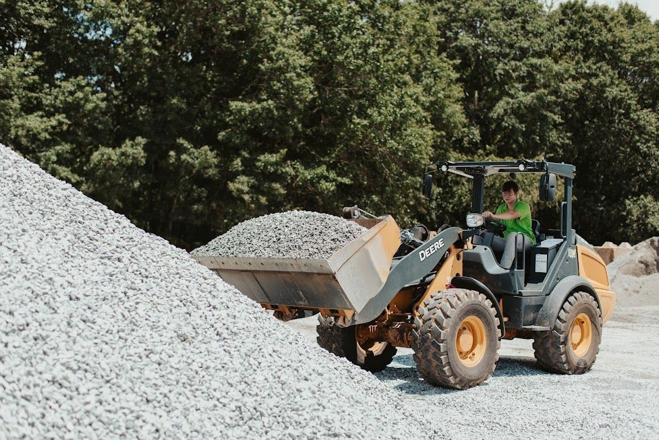 A person operates a yellow front-end loader to move a pile of gravel in a quarry.