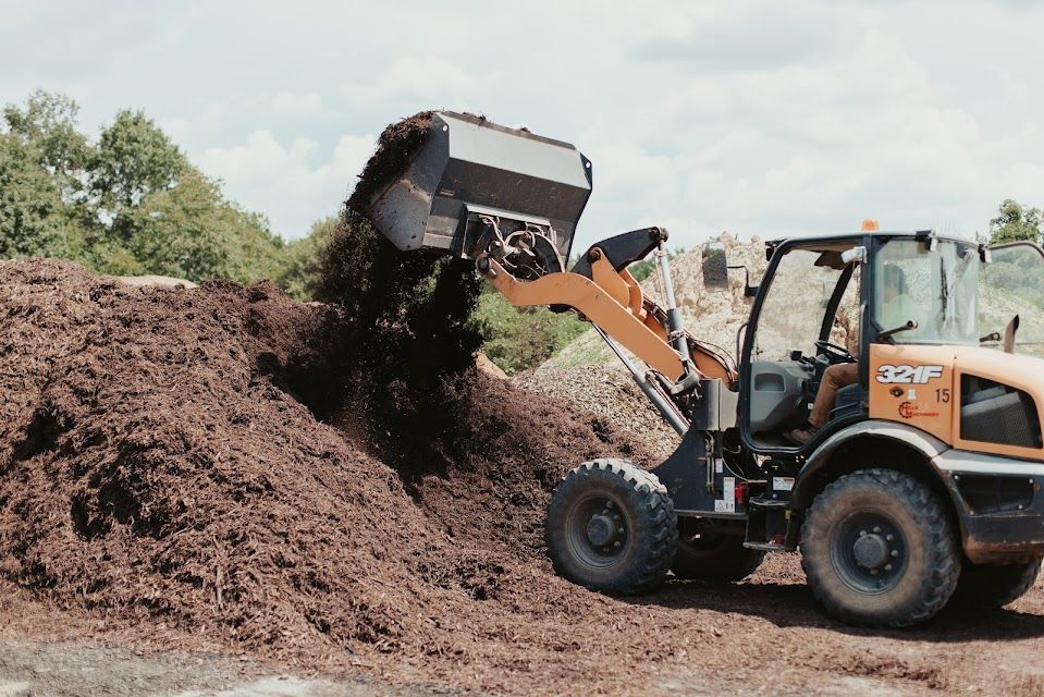 Small orange Case loader dumping mulch onto a large pile on a sunny day.