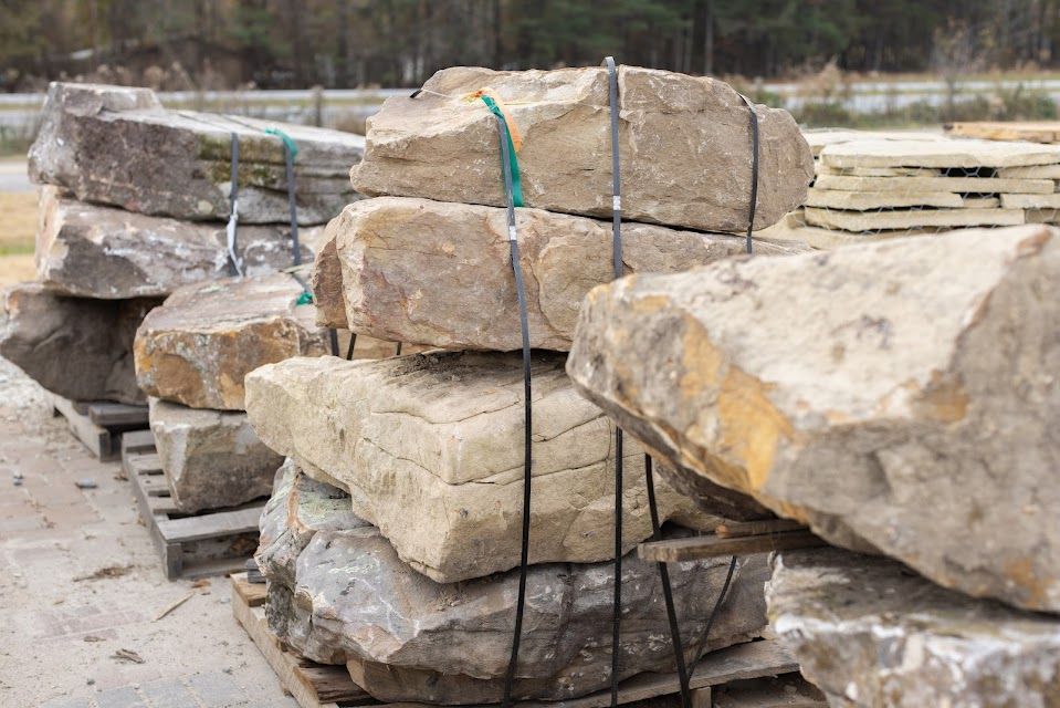 Stacks of large, light-colored landscaping stones bound with green strapping on wooden pallets.