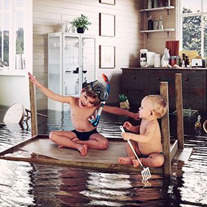 Two children are sitting on a raft in a flooded room.