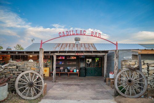 A building with a sign that says `` cadillac bar '' and wagon wheels in front of it.