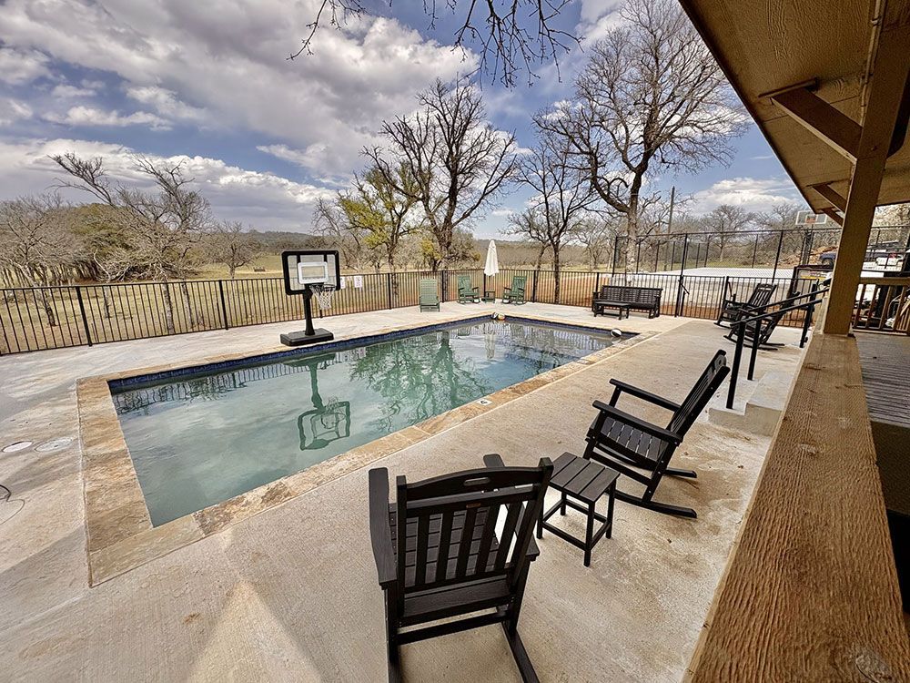 A large swimming pool surrounded by rocking chairs and tables.