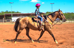 A young girl is riding a horse in a dirt field.