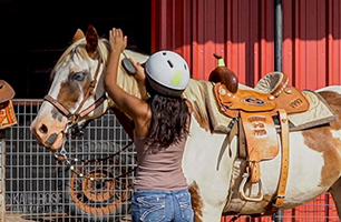 A woman is petting a brown and white horse in a stable.