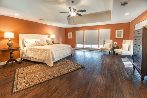 A bedroom with hardwood floors, a bed, chairs, a dresser and a ceiling fan.