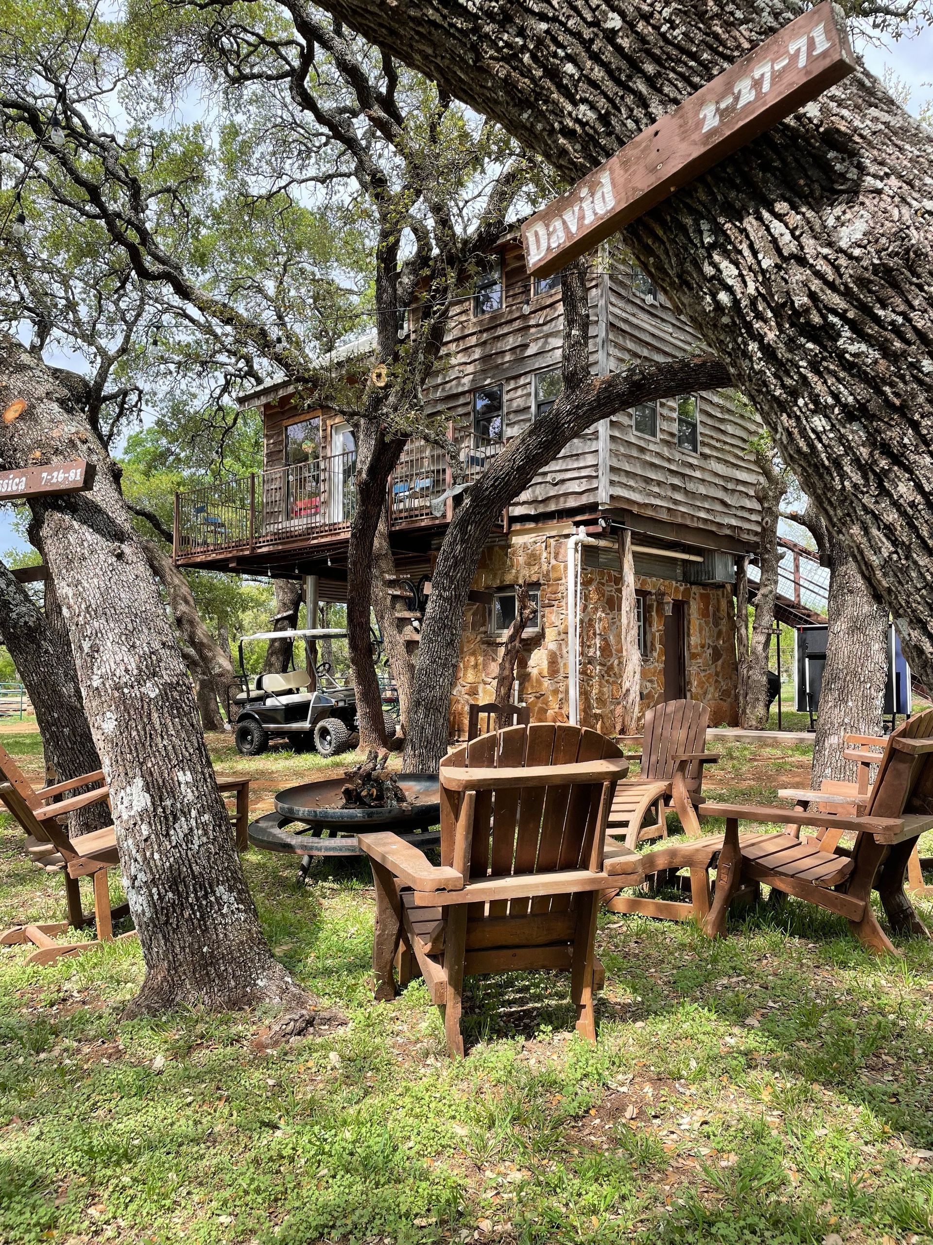 A tree house is surrounded by wooden chairs and trees.