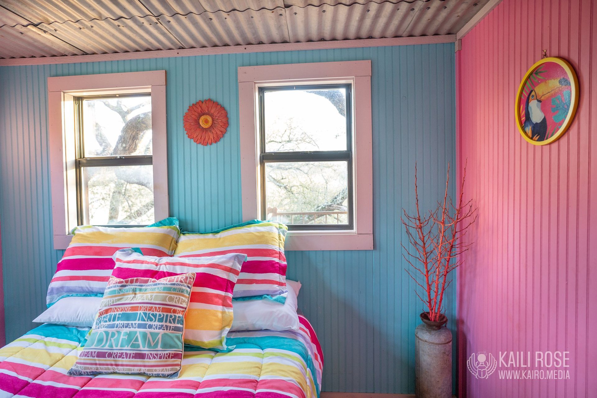 A bedroom with a bed, two windows, and a painting on the wall.
