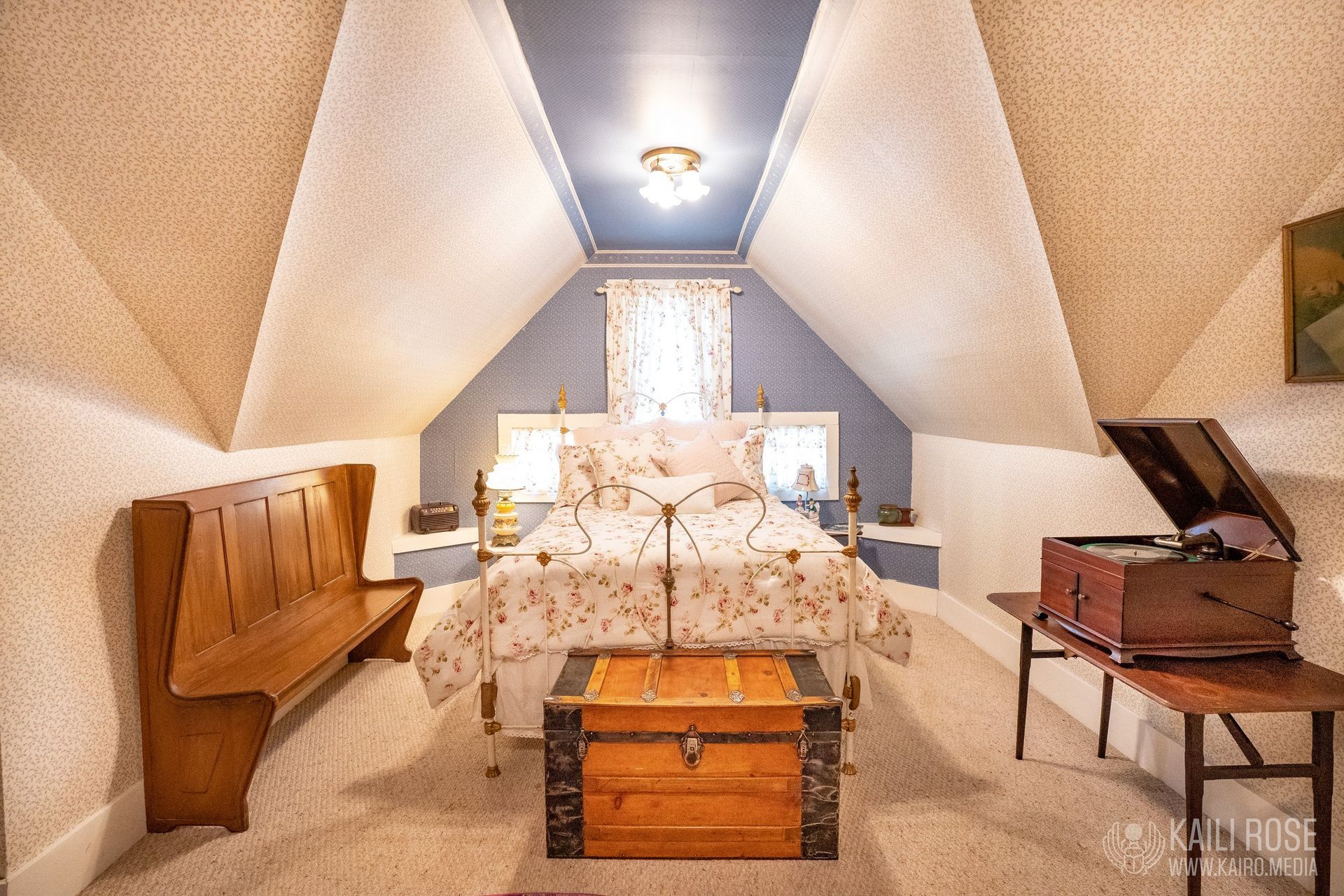 A bedroom with a bed, trunk, bench and record player.