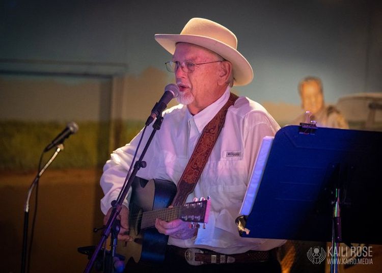 A man in a hat is playing a guitar and singing into a microphone.