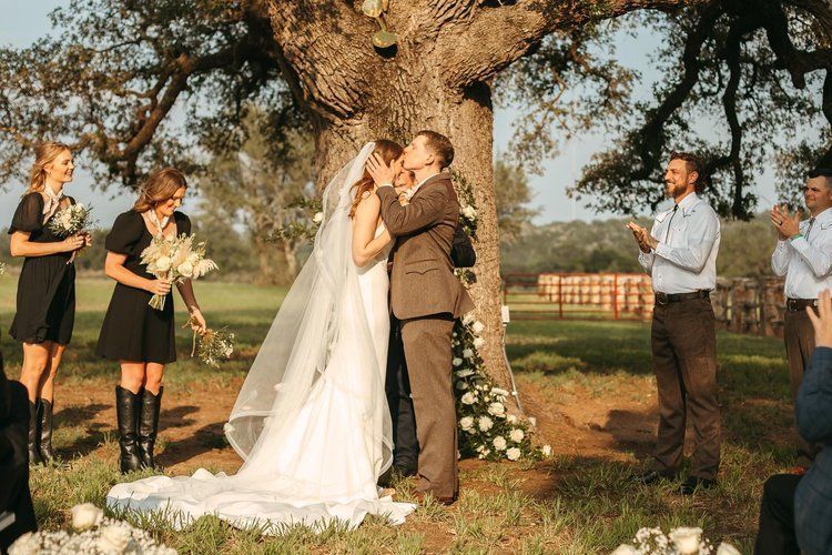 A bride and groom kissing under a tree at their wedding ceremony.