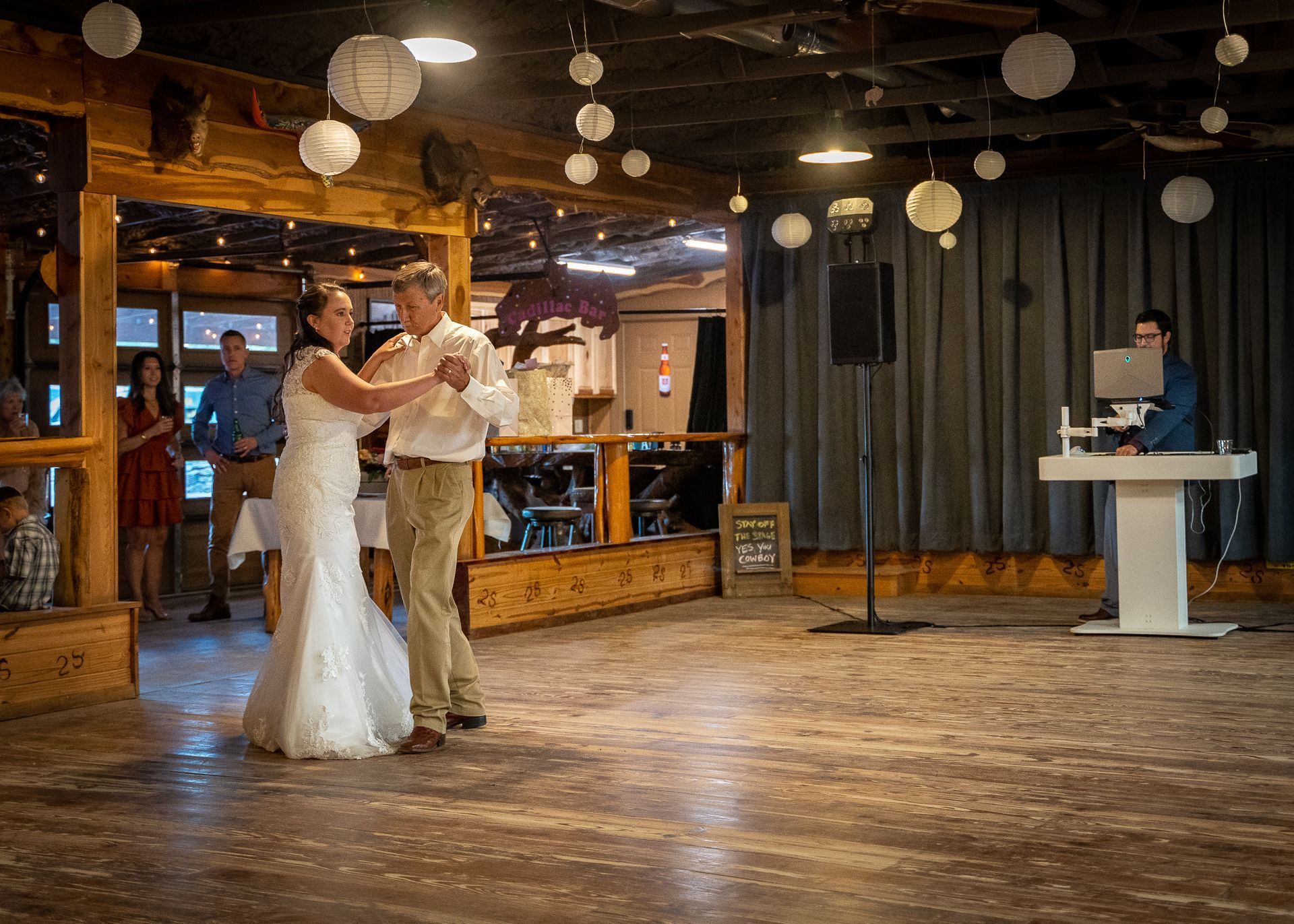 A bride and groom are dancing in a room with a dj playing music.