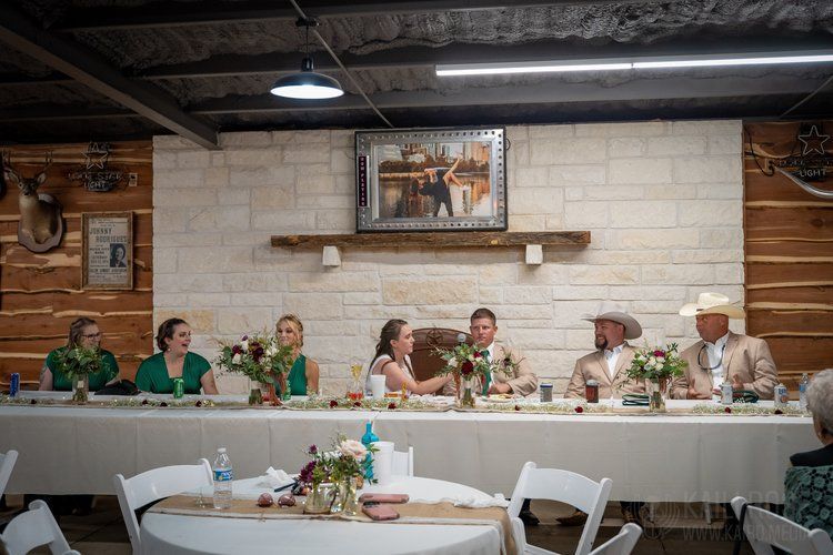 A group of people are sitting at a long table at a wedding reception.