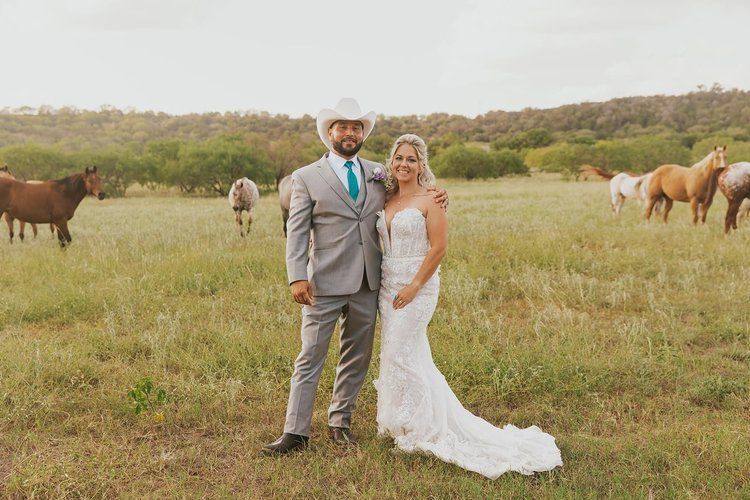 A bride and groom are posing for a picture in a field with horses.