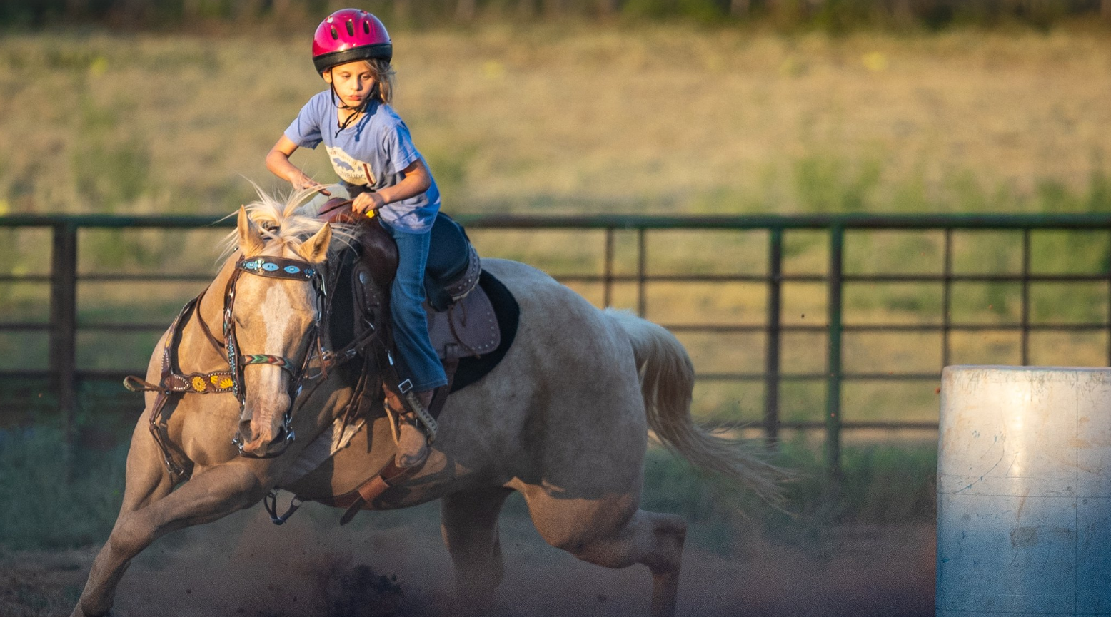 A young boy is riding a horse around a barrel.