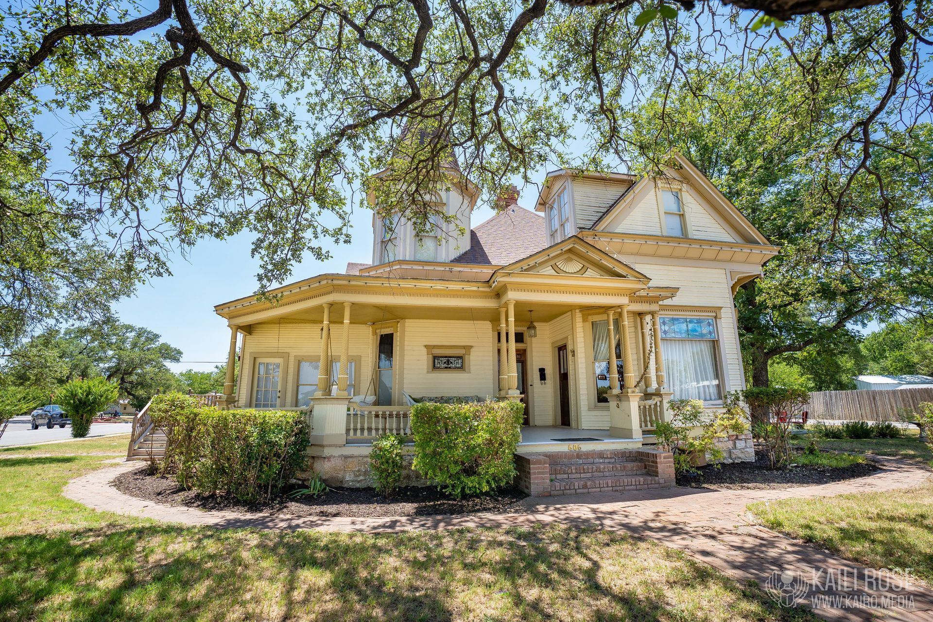A large yellow house with a large porch is surrounded by trees.