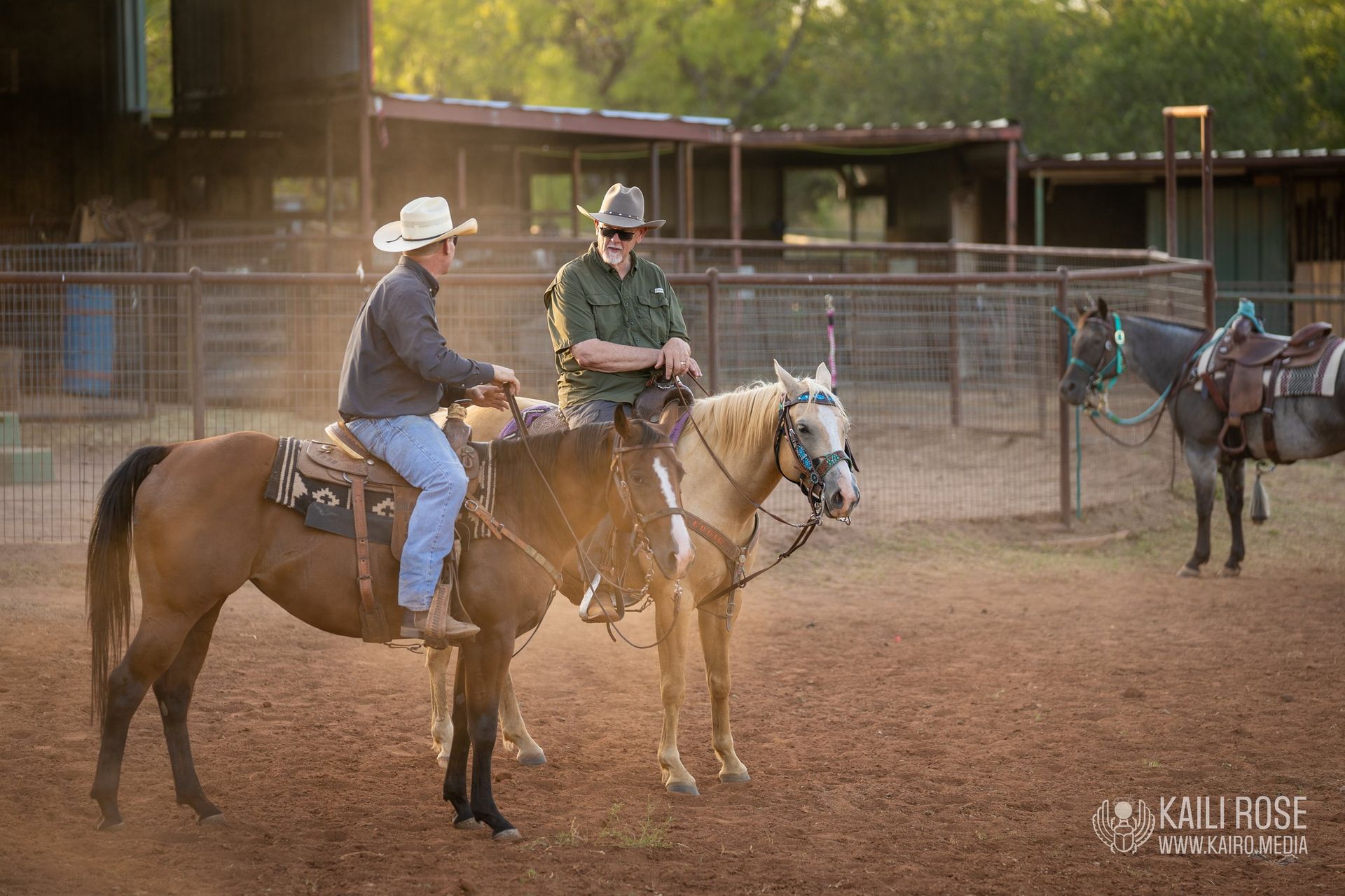 Two men are riding horses in a fenced in area.