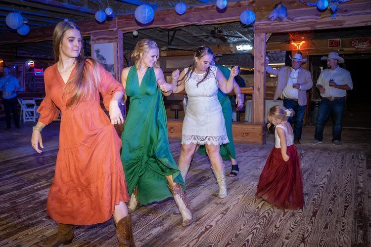 A group of women are dancing on a wooden floor at a wedding reception.