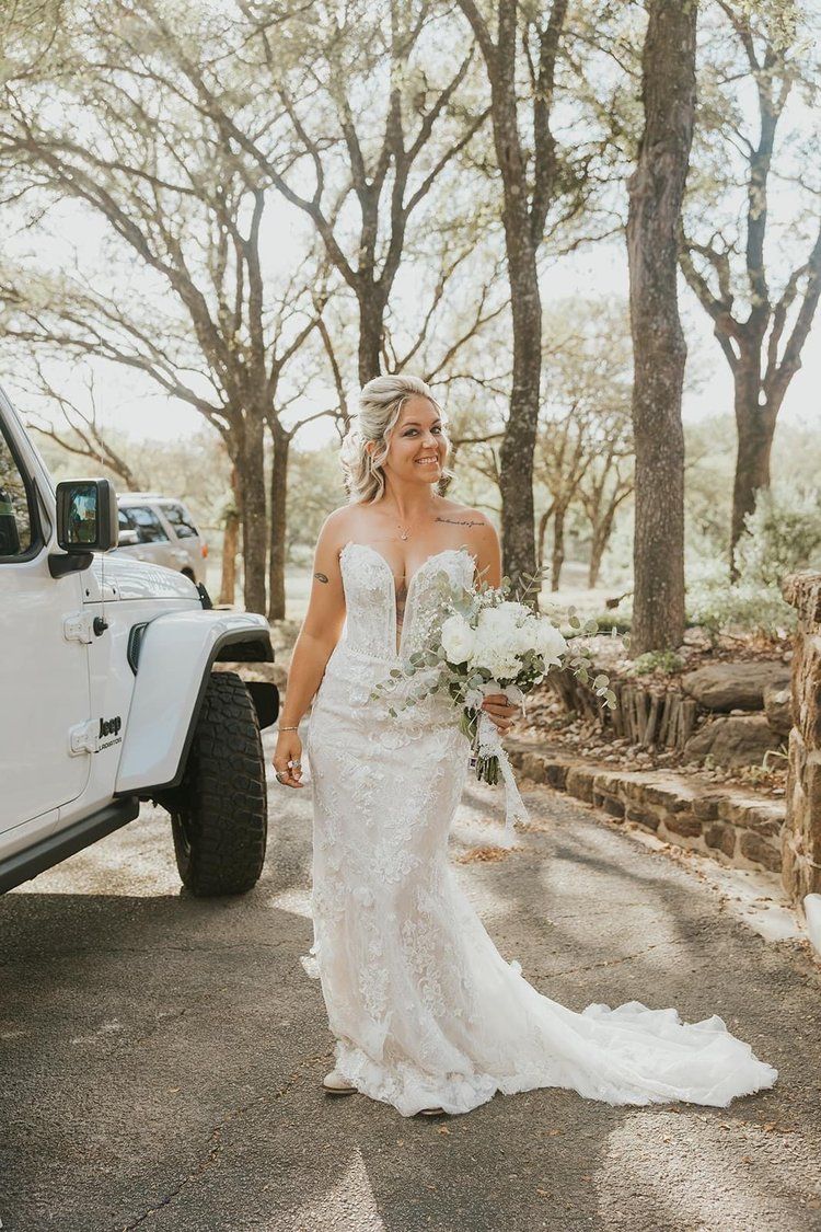 A bride in a wedding dress is standing in front of a white jeep.