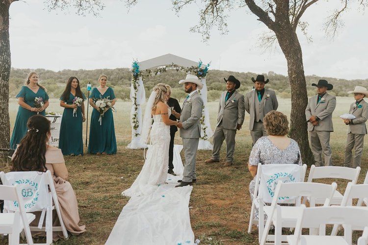 A bride and groom are holding hands during their wedding ceremony while their wedding party watches.