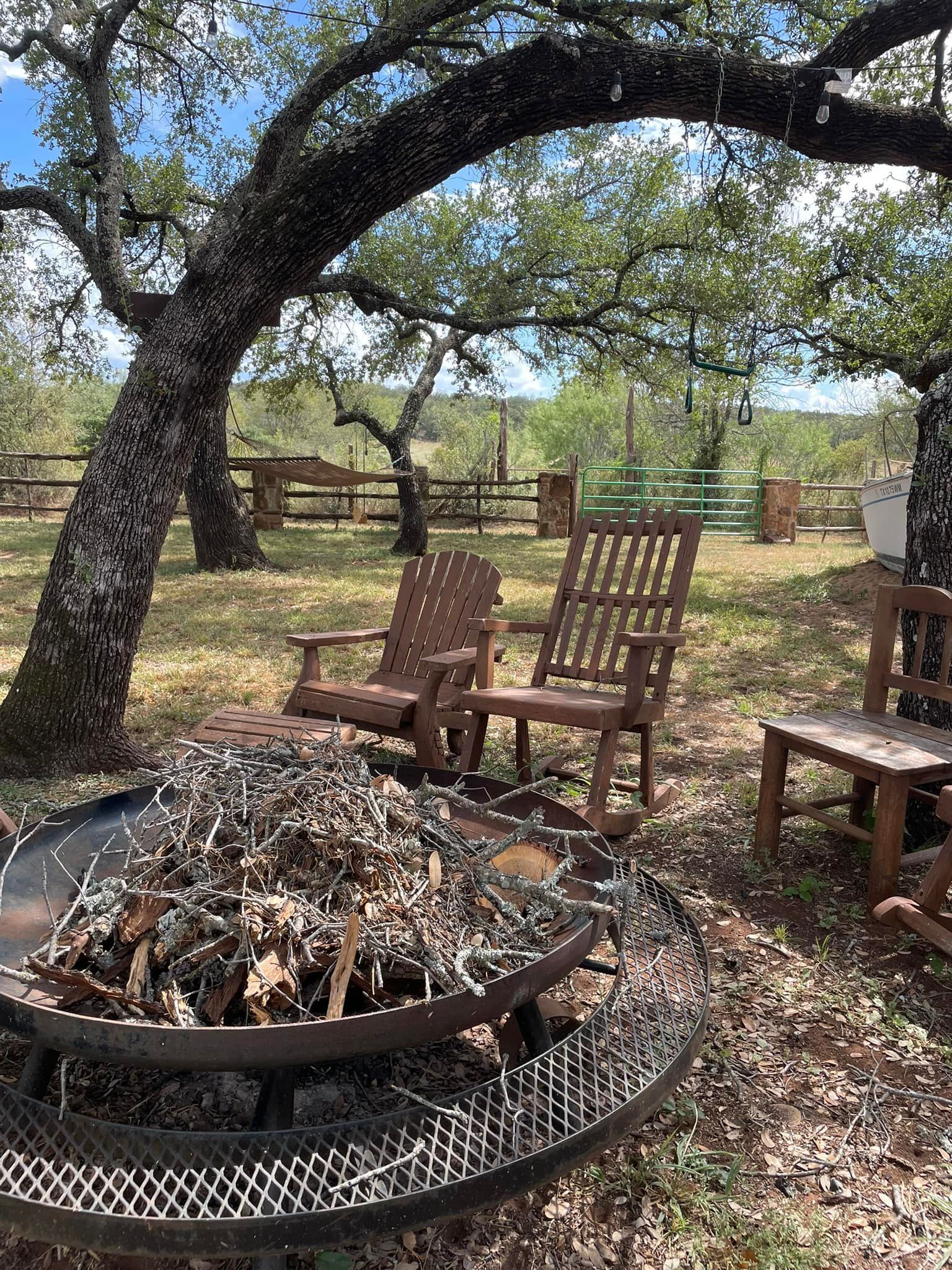 A fire pit surrounded by chairs and trees in a field.