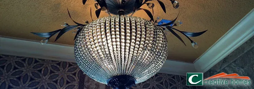 Crystal chandelier with black accents against a patterned wallpaper and gold-toned ceiling.