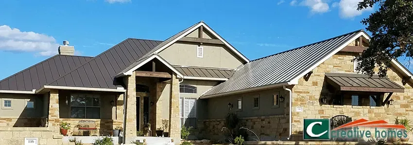 A large, modern house with stone and stucco exterior, dark roof, and blue sky.