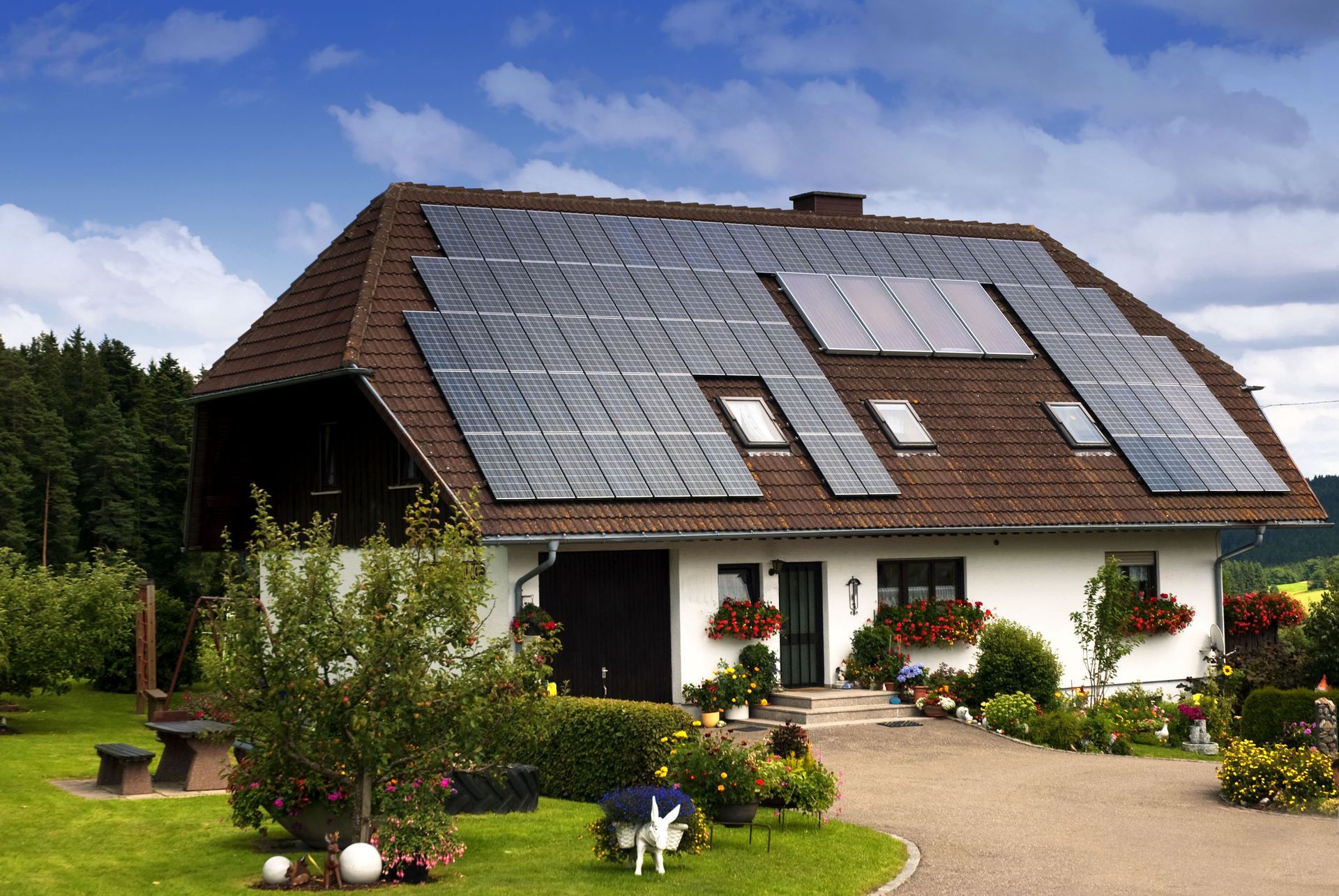 House with solar panels on a brown roof, surrounded by a garden and a blue sky.