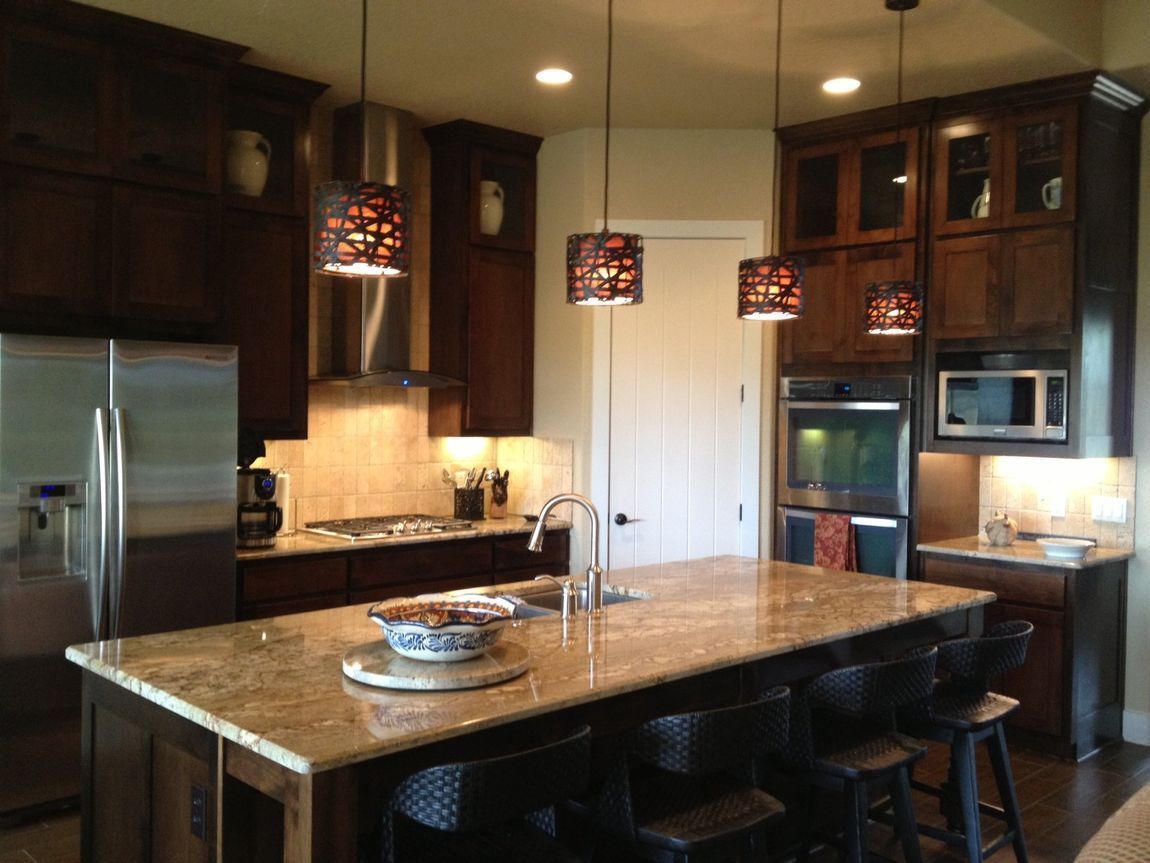 A well-lit kitchen with dark wooden cabinets, a granite countertop island, and pendant lights.