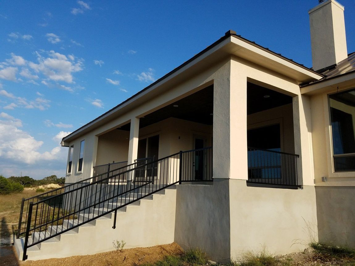Beige stucco house with porch and black railing against a blue sky.
