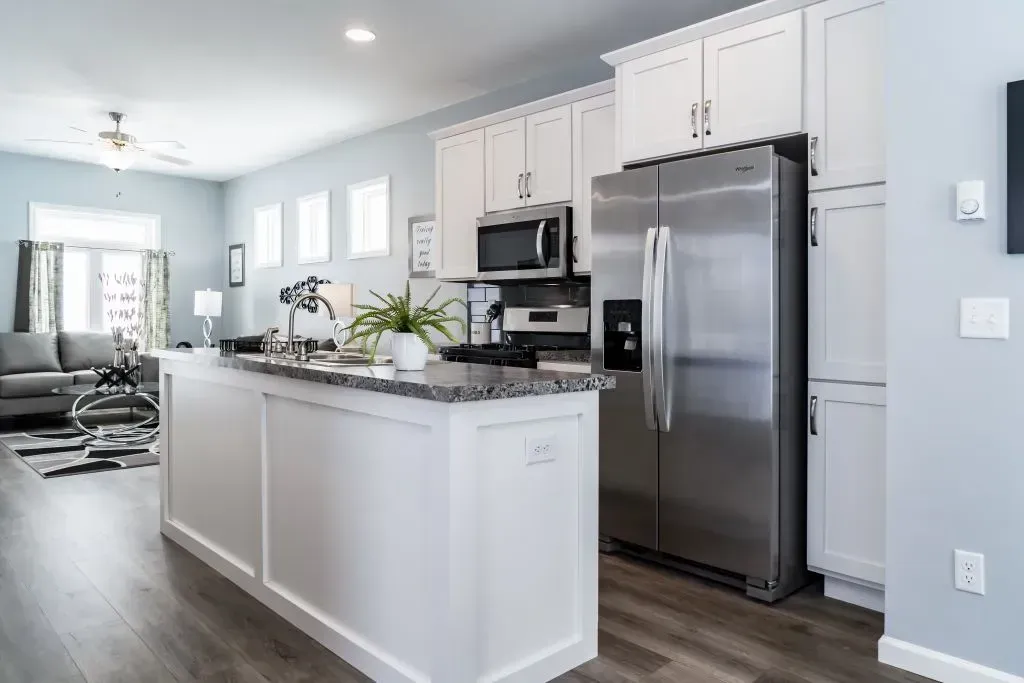 Open-concept kitchen with white cabinets, stainless steel appliances, and gray countertop island.